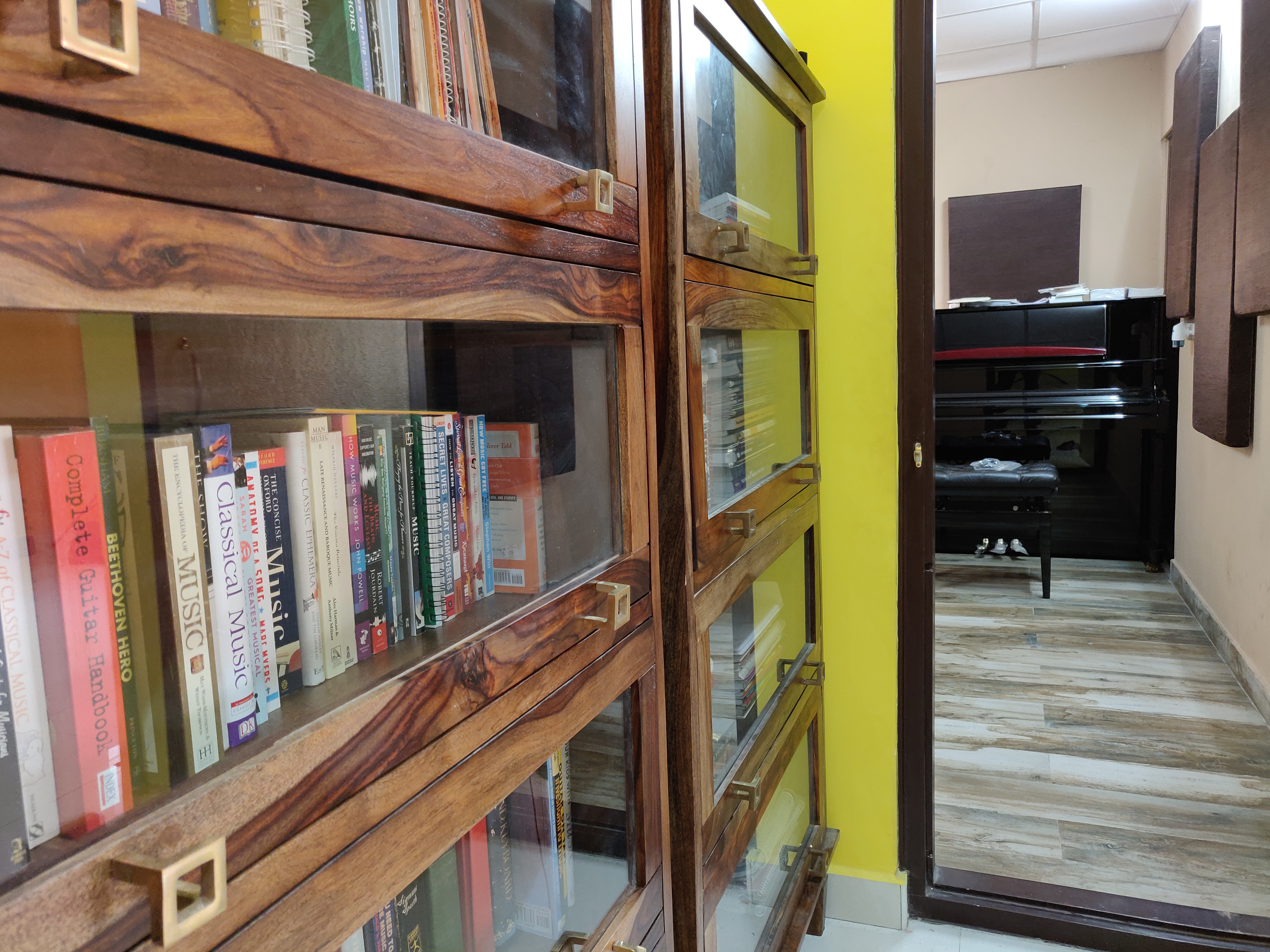 FSG music library — glass-fronted book cabinet with classical music books, scales and theory workbooks, exam room piano in background