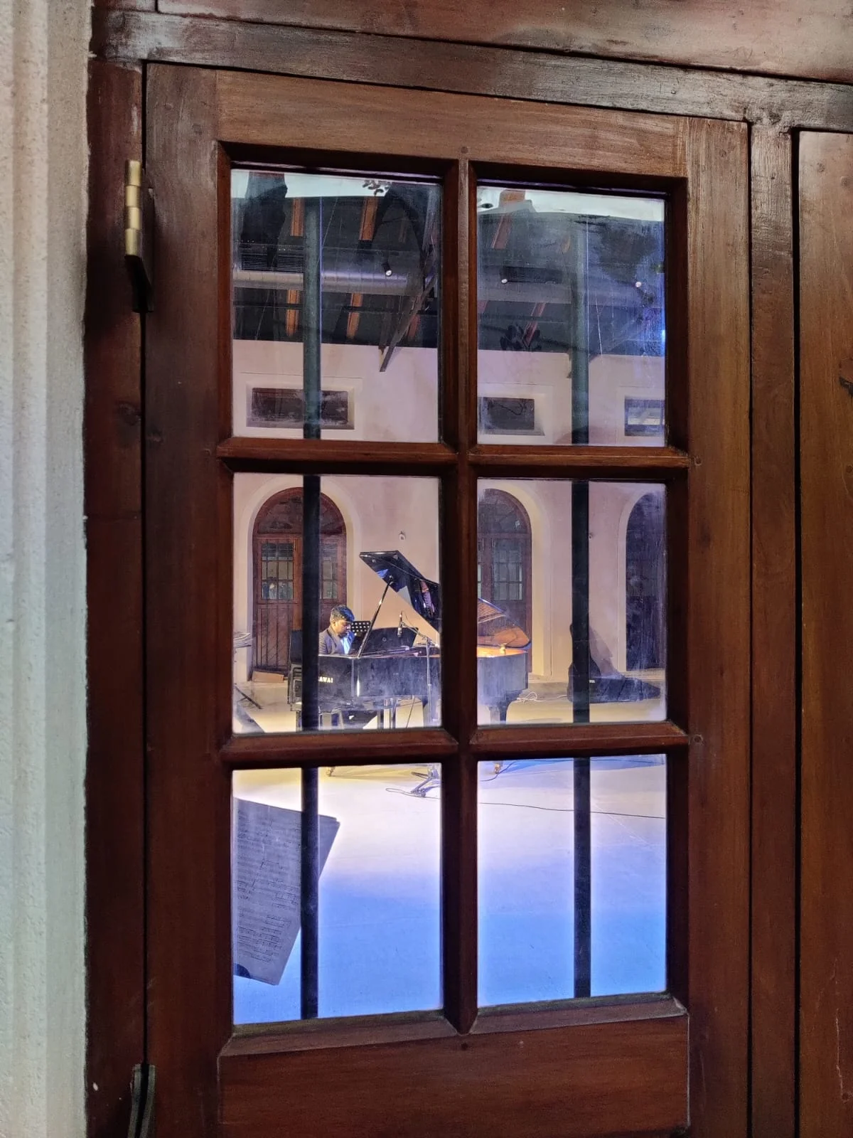 FSG pianist performing at The Sabha Bangalore — seen through the old wooden door